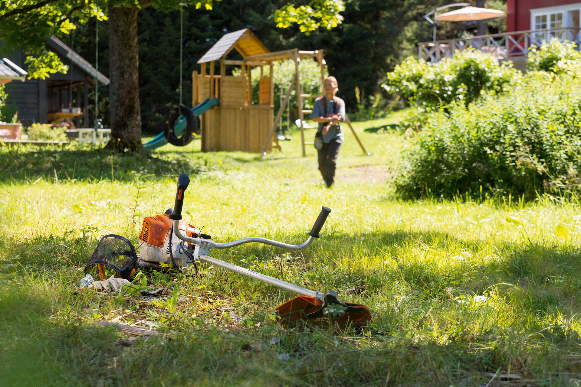 A STIHL FS 240 brushcutter in grass with a man preparing for maintenance in the background
