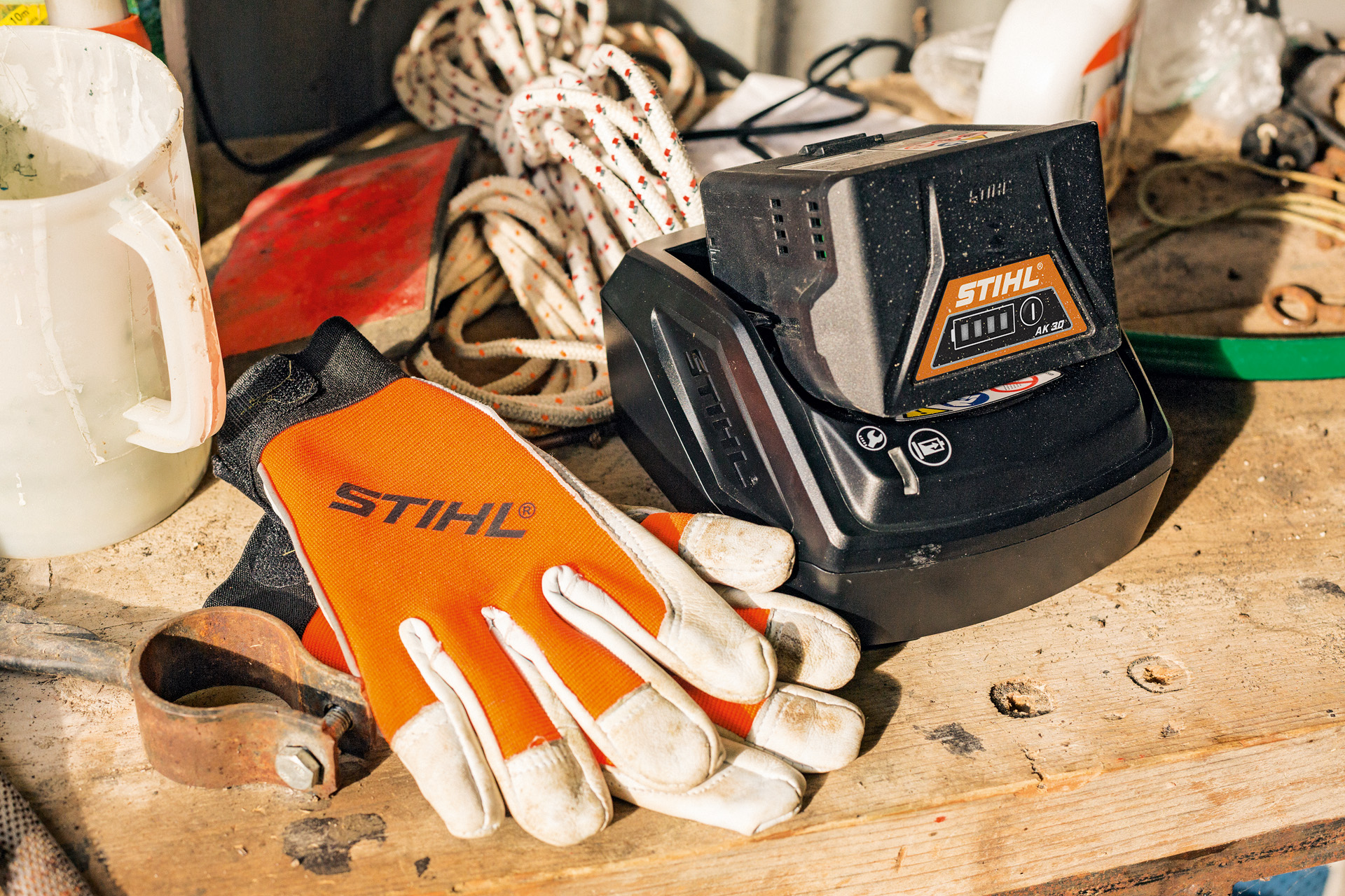 AK-Series lithium-ion batteries charging alongside STIHL gloves and tools