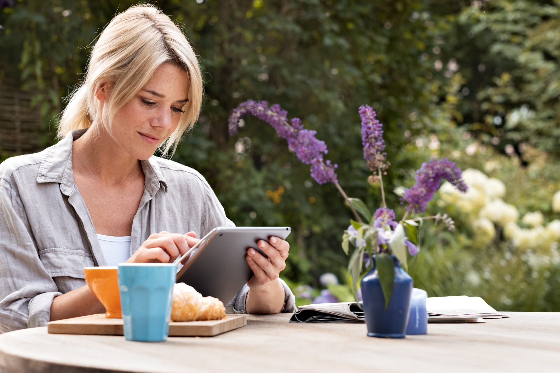 A woman using a tablet at a breakfast table in a garden